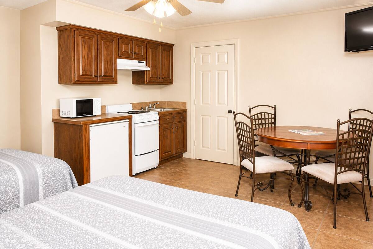 A compact kitchen with a microwave, stove, and sink, a dining table with chairs, and a TV mounted on the wall.