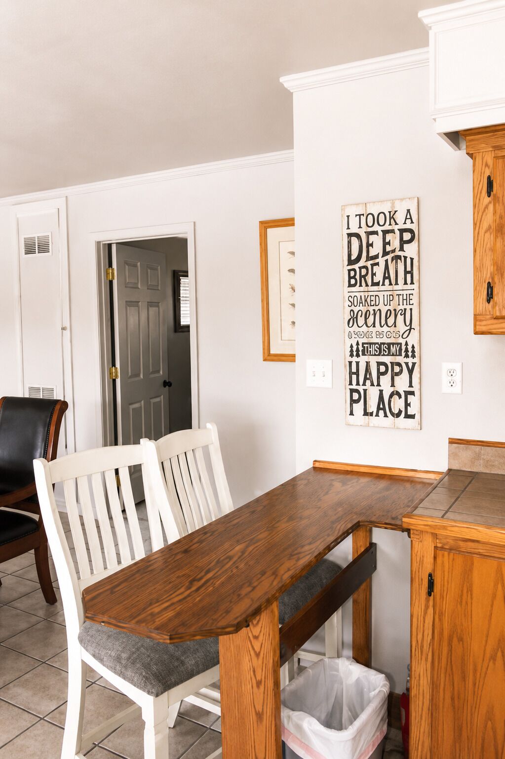 A dining area with a wooden table and chairs, a kitchen counter, and a wall-mounted sign.