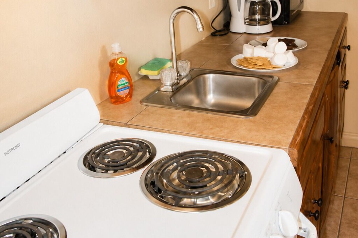 A kitchen with a white stove, a sink, wooden cabinets, a coffee maker, and a dish rack.
