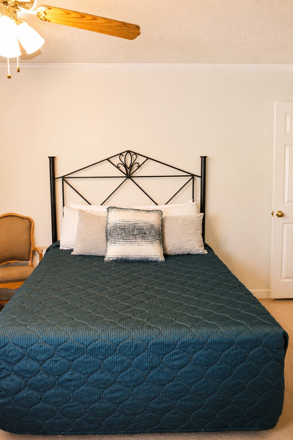 A bed with a dark quilted cover, a metal headboard, and two pillows.