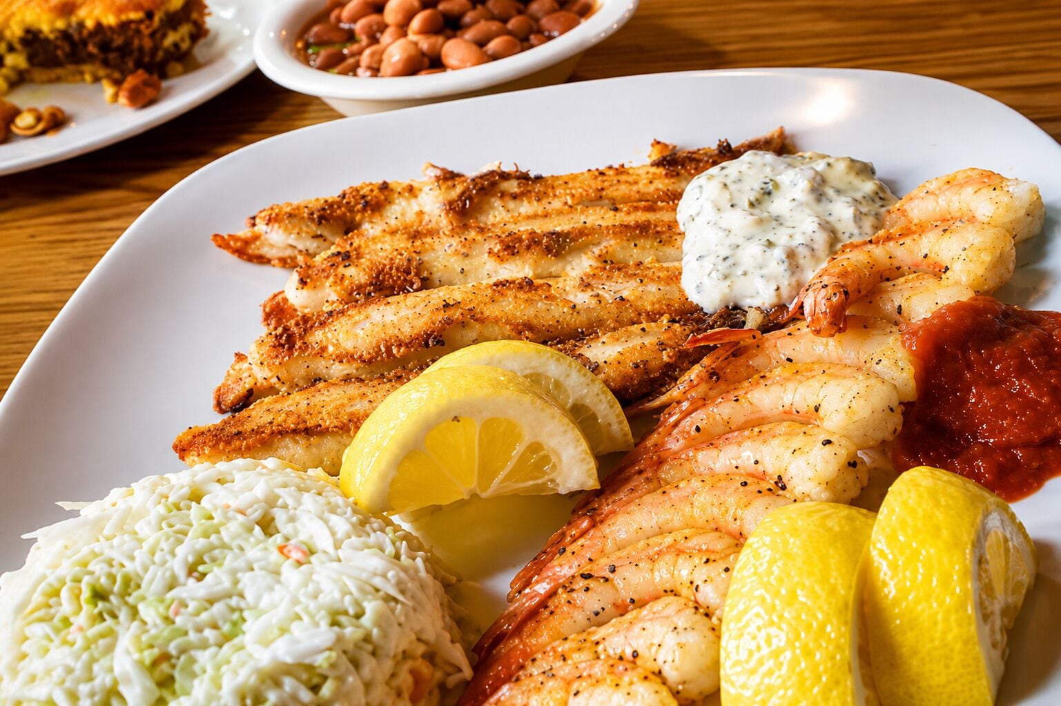 Une assiette de poisson grillé, de crevettes, de salade de chou et de quartiers de citron.
