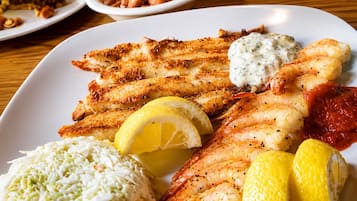 Um prato com peixe grelhado, camarões, salada de repolho e gomos de limão.