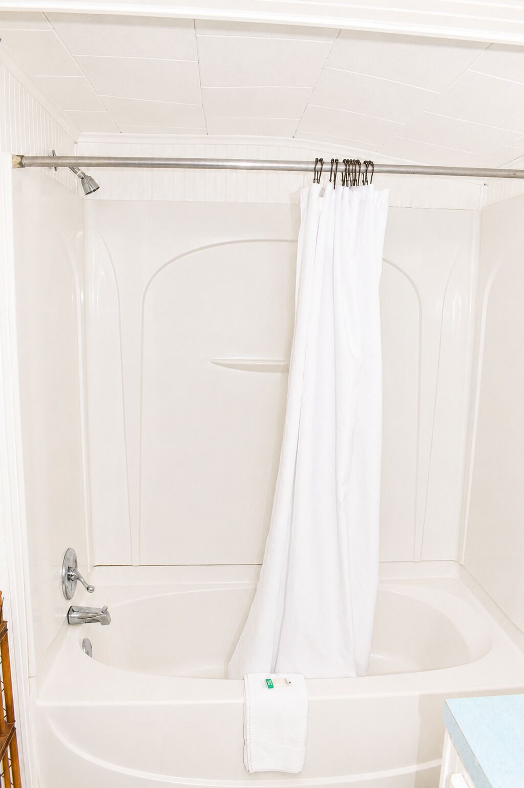 A white bathtub with a shower curtain, a towel, and a green object on the edge.