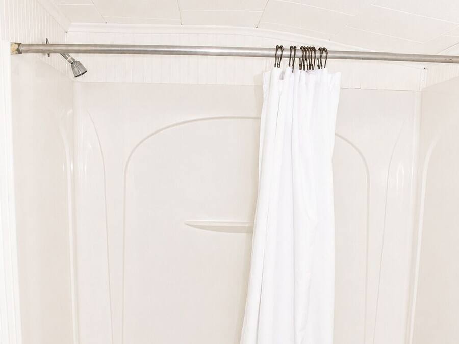 Una bañera blanca con cortina de ducha, una toalla y un objeto verde en el borde.