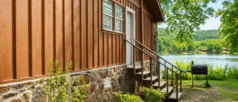 A cabin with a stone foundation, wooden exterior, a staircase, and a view of a lake.