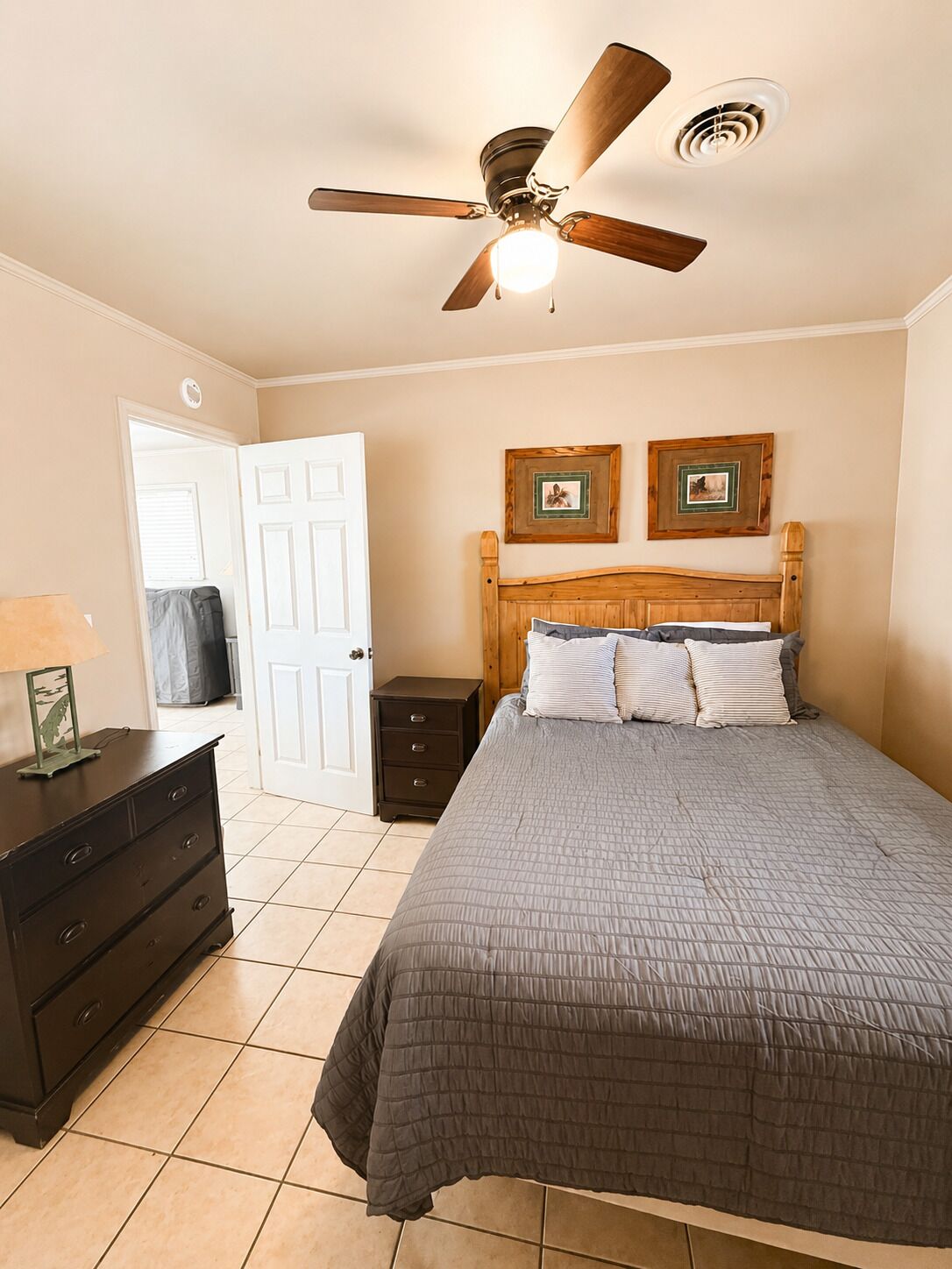 A bedroom with a bed, a nightstand, a dresser, a ceiling fan, and two framed pictures on the wall.
