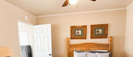A bedroom with a bed, a nightstand, a dresser, a ceiling fan, and two framed pictures on the wall.
