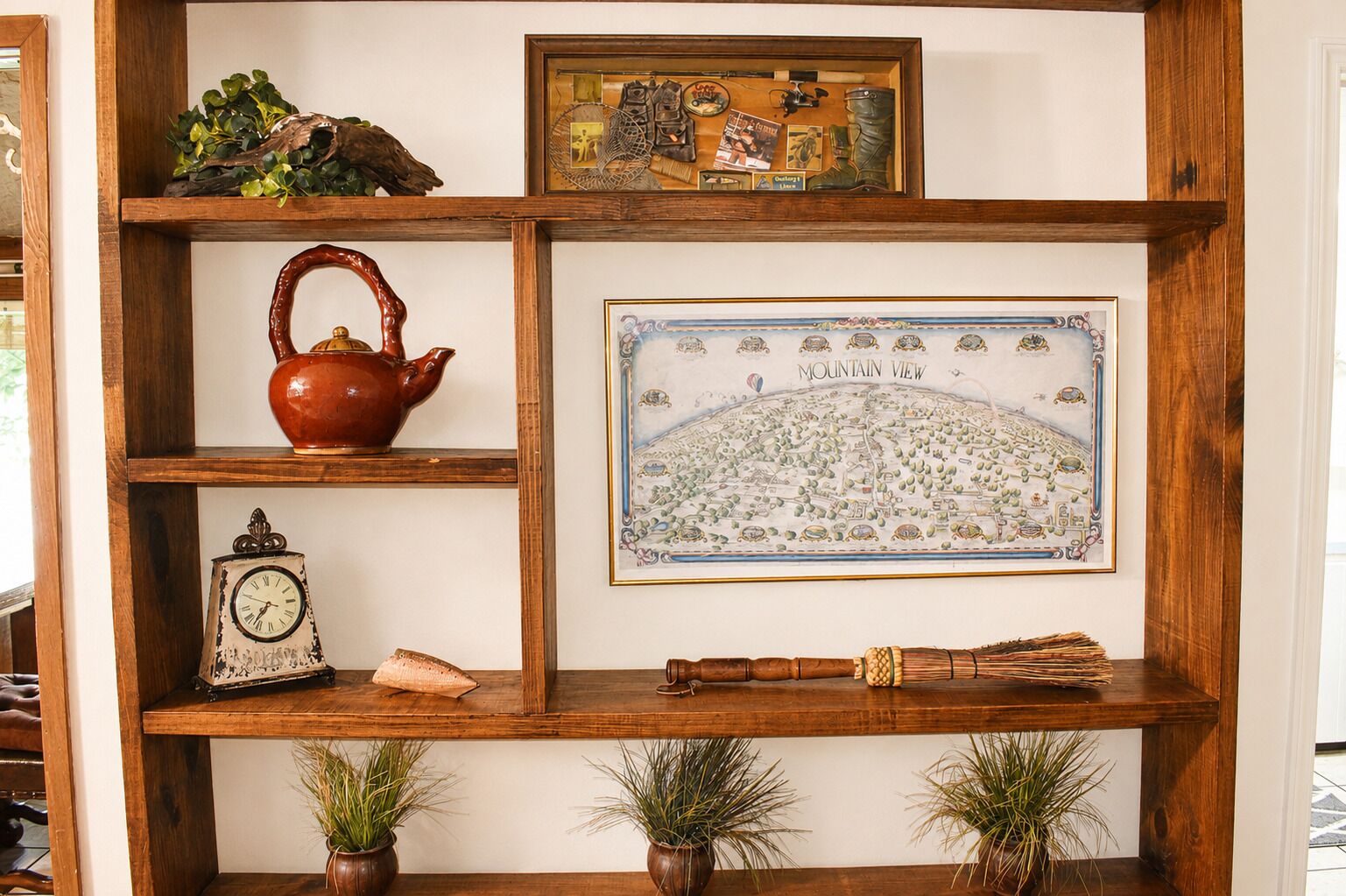 A wooden shelf unit with a framed map, a clock, a teapot, and small potted plants.