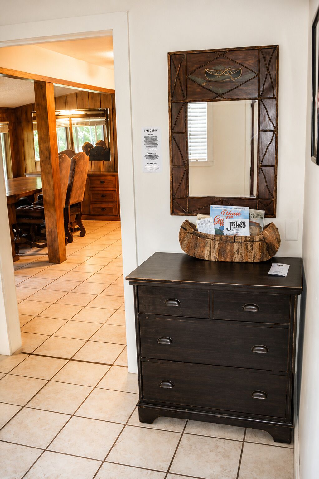 A dark wooden dresser with a mirror above it, a wooden bowl with magazines, and a sign on the wall.