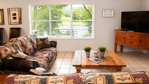 A living room with a sofa, a coffee table, a TV, and a window with blinds. - Jack's White River Fishing Resort (Mountain View)
