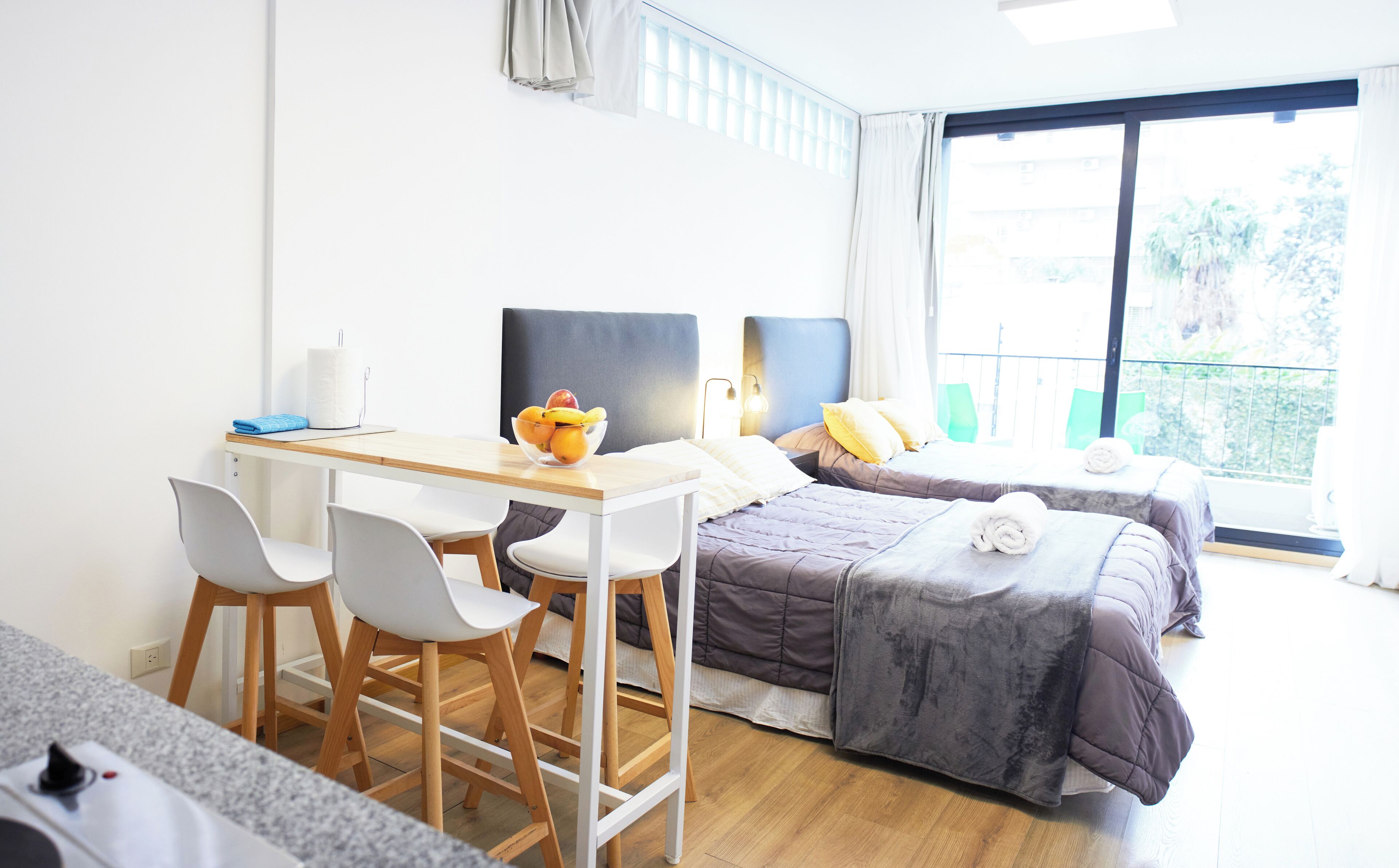 Habitación de hotel con escritorio, dos camas, ventana con vistas y un balcón pequeño.