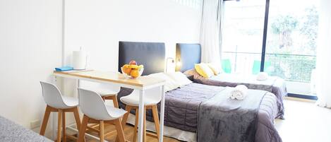 Habitación de hotel con escritorio, dos camas, ventana con vistas y un balcón pequeño.
