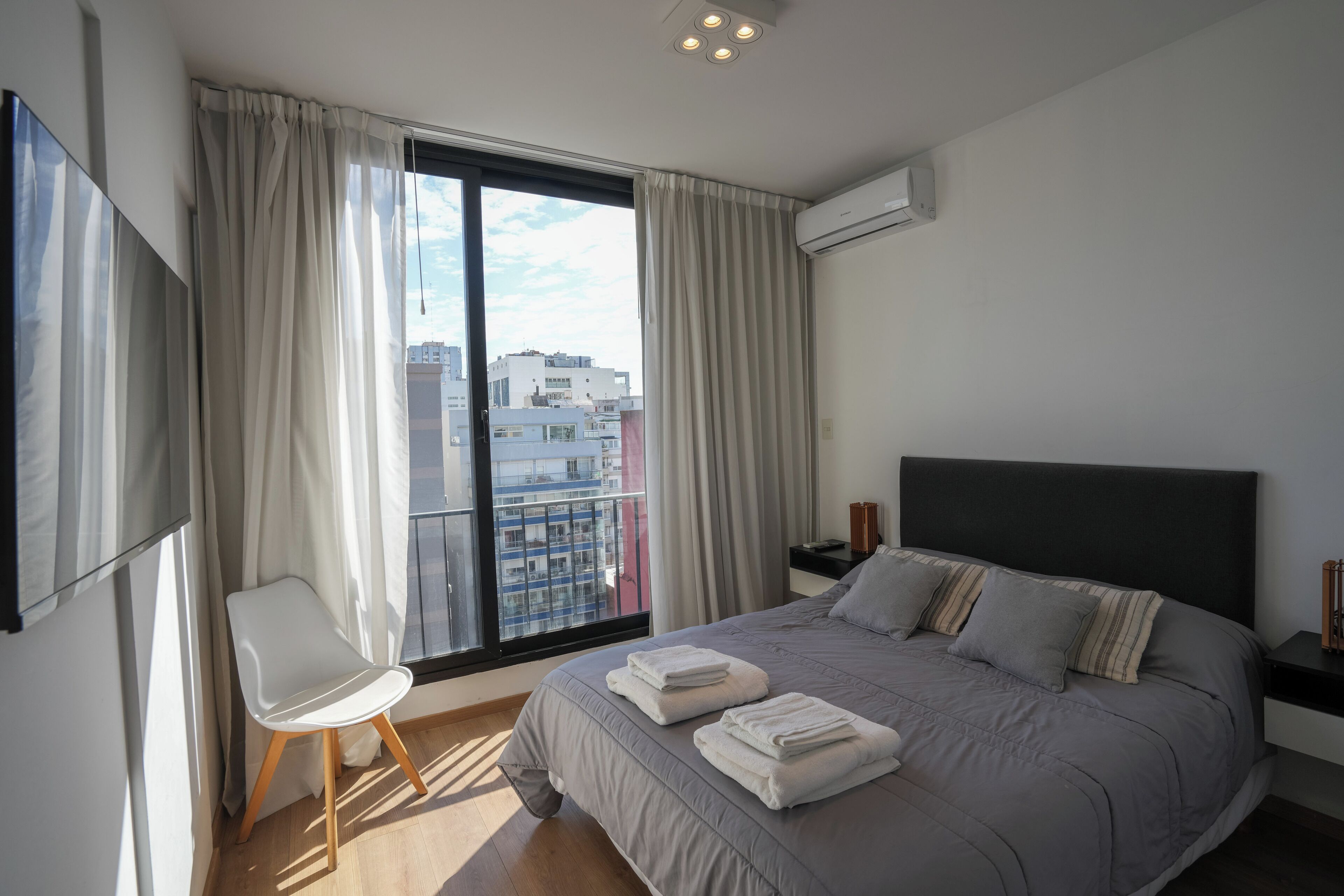 Camera da letto moderna con un letto grande, una poltrona e vista sulla città attraverso un'ampia finestra.