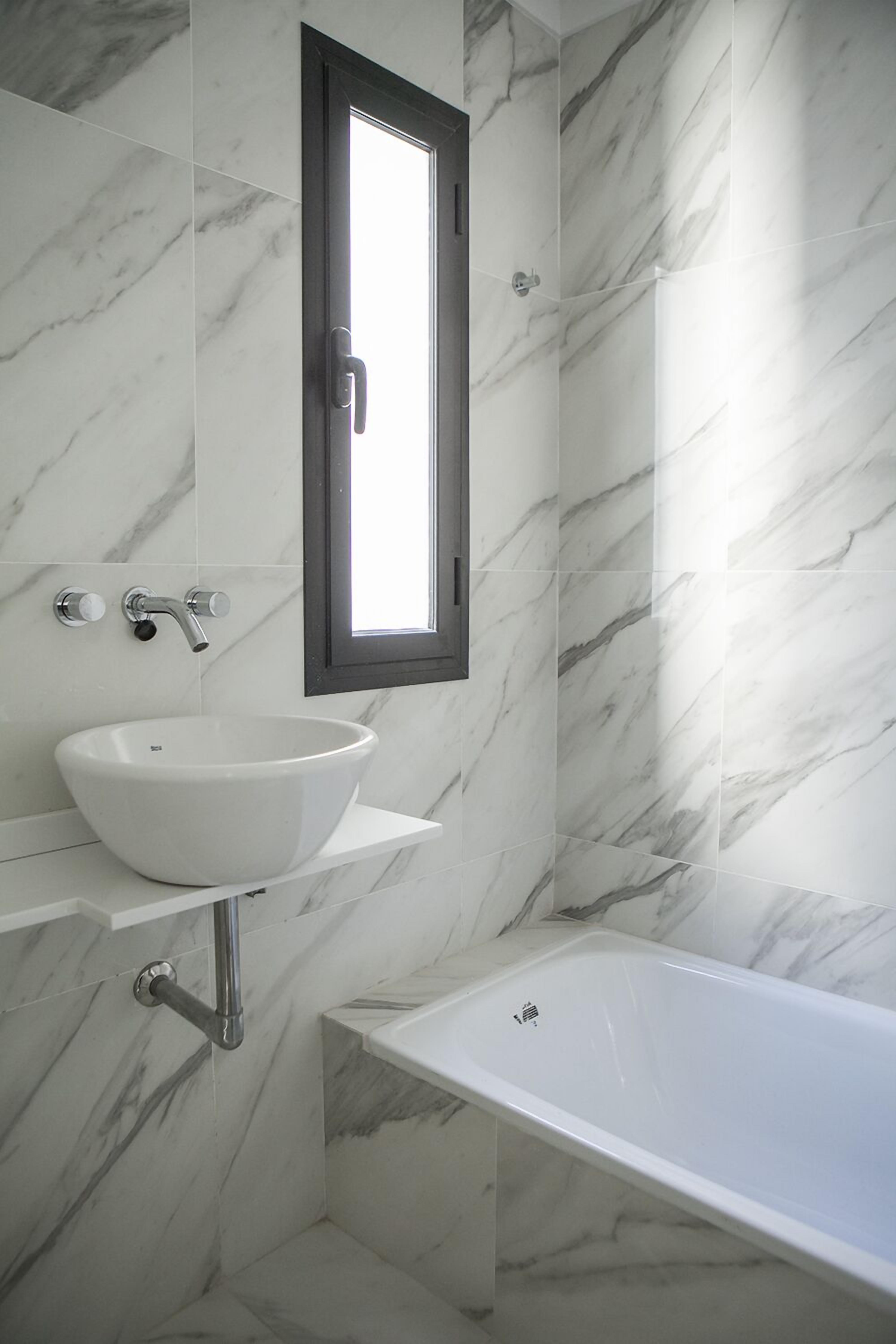 A modern bathroom with a white marble sink, a bathtub, and a window above the sink.