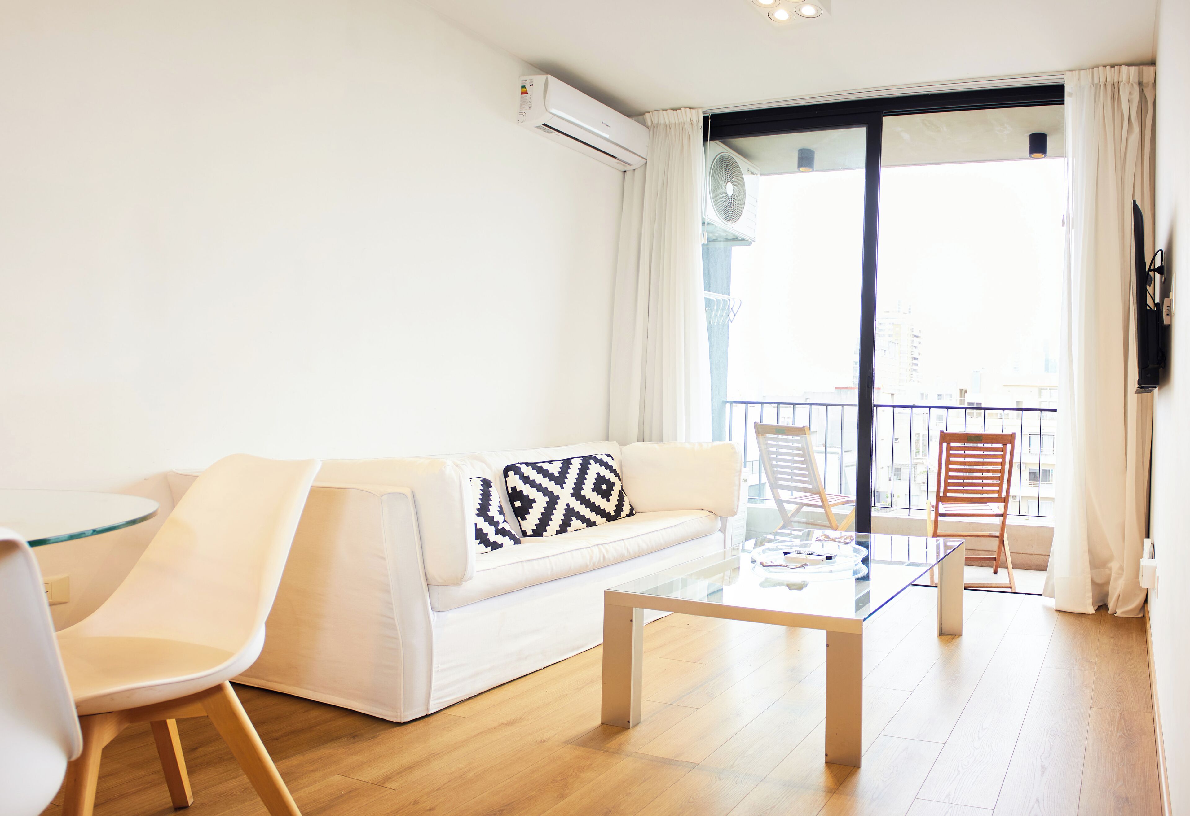 A modern living room with a white sofa, a glass coffee table, and a wooden floor.