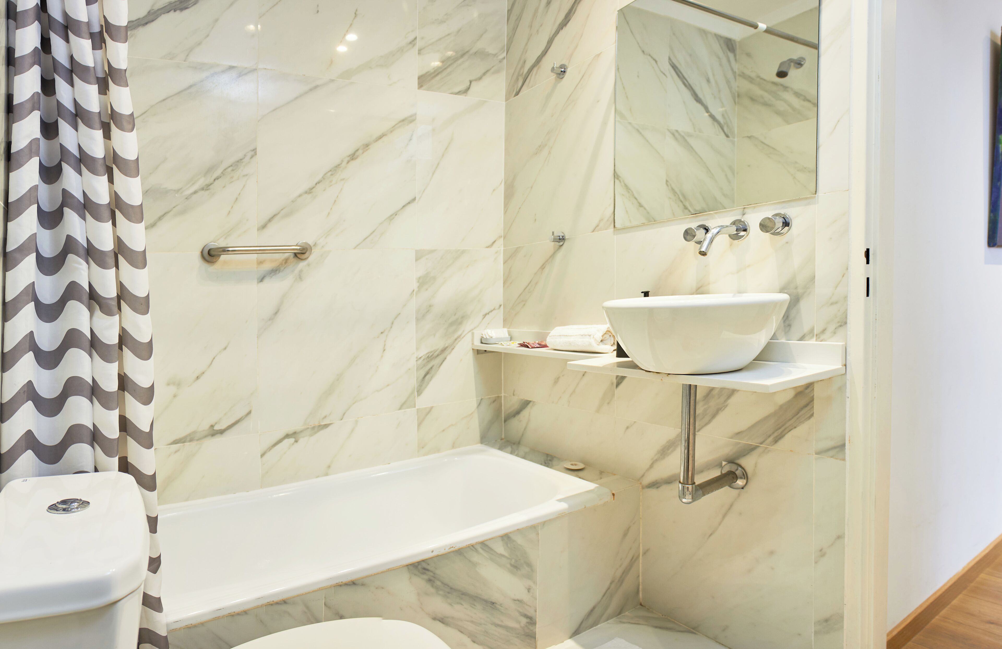 A bathroom with a white bathtub, a white sink with a marble countertop, and a shower area with a glass door.