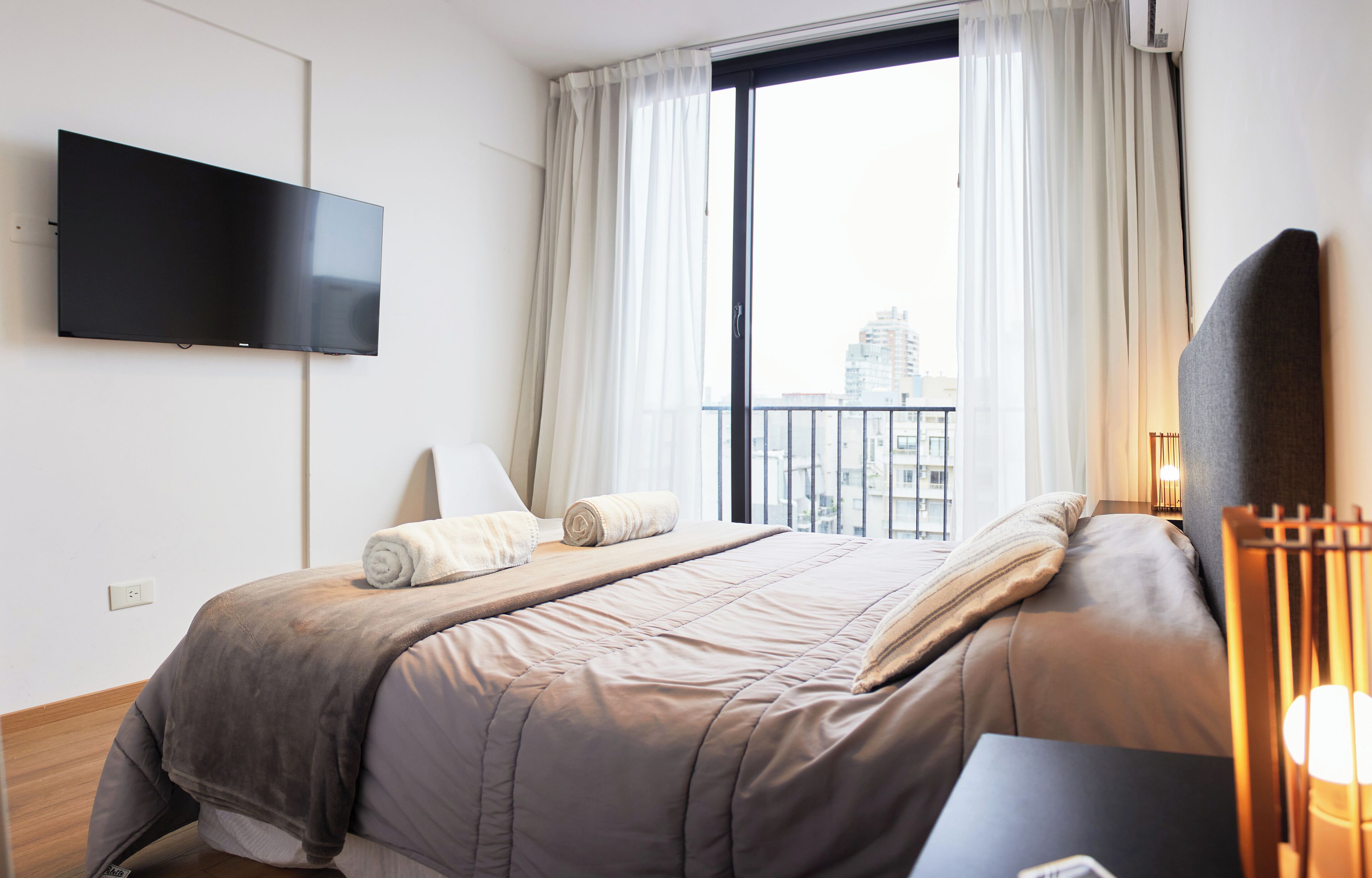 Una camera d'albergo moderna con un letto grande, una TV a schermo piatto montata a parete e un balcone con tende.