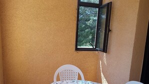 Eine kleine Terrasse mit einem runden Tisch, bedeckt mit einer blumigen Tischdecke, umgeben von weißen Plastikstühlen.
