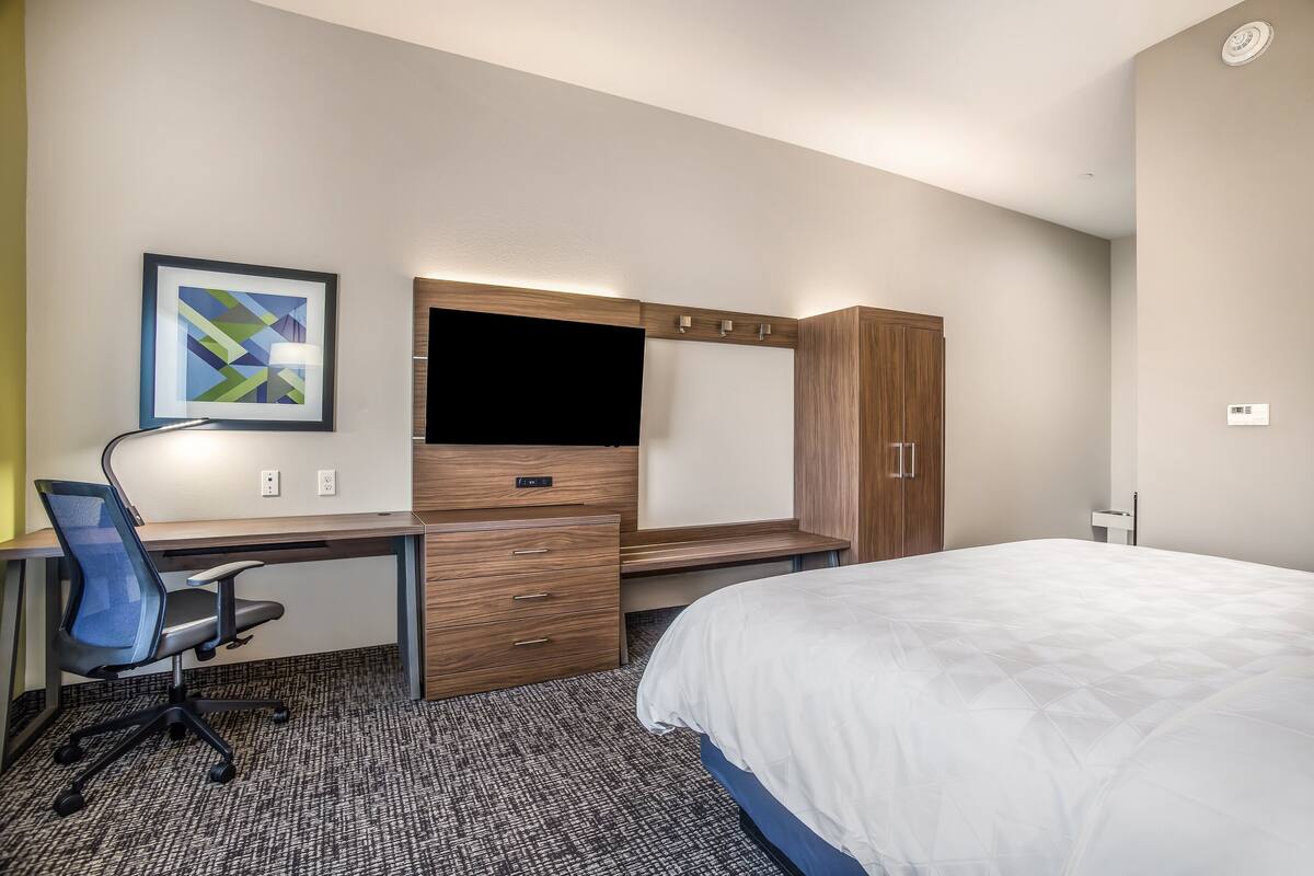 Una habitación de hotel moderna con cama, escritorio, silla, televisor y armario.