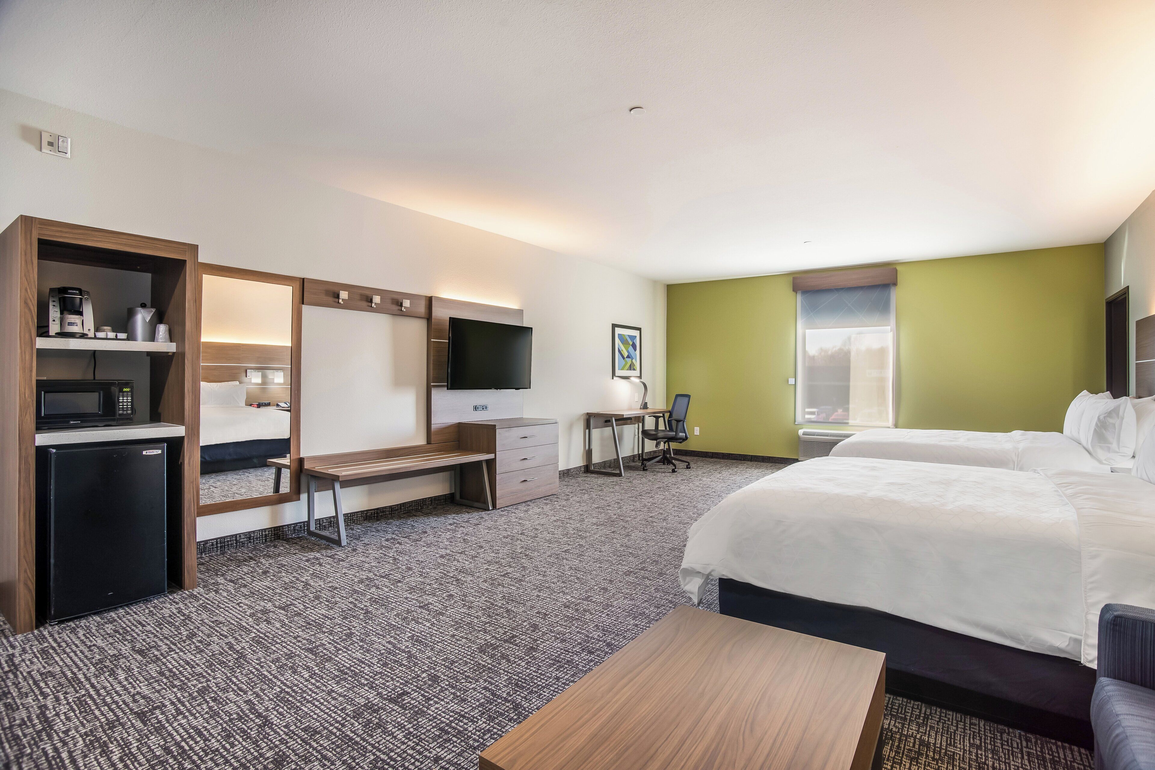 A hotel room with a bed, desk, chair, and a small kitchenette.
