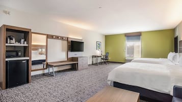 A hotel room with a bed, desk, chair, and a small kitchenette.