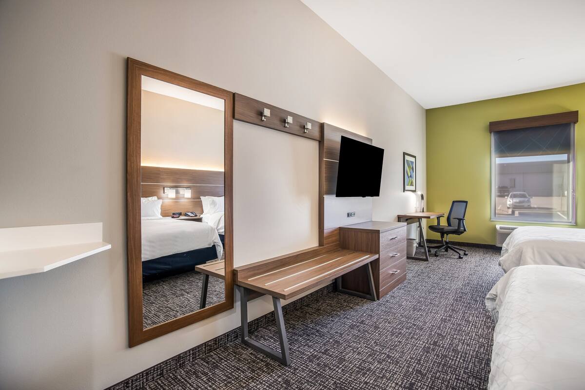 Habitación de hotel con cama, escritorio, silla, televisor y un espejo grande.
