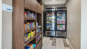 A hallway with a wooden shelf stocked with snacks and a double-door refrigerator with beverages. - Holiday Inn Express & Suites Tulsa East - Catoosa by IHG (Tulsa)