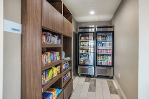 A hallway with a wooden shelf stocked with snacks and a double-door refrigerator with beverages. - Holiday Inn Express & Suites Tulsa East - Catoosa by IHG (Tulsa)