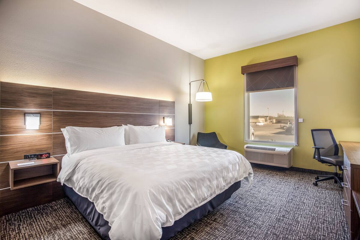 Una habitación de hotel con una cama grande, mesitas de noche, un escritorio y una ventana con vistas.