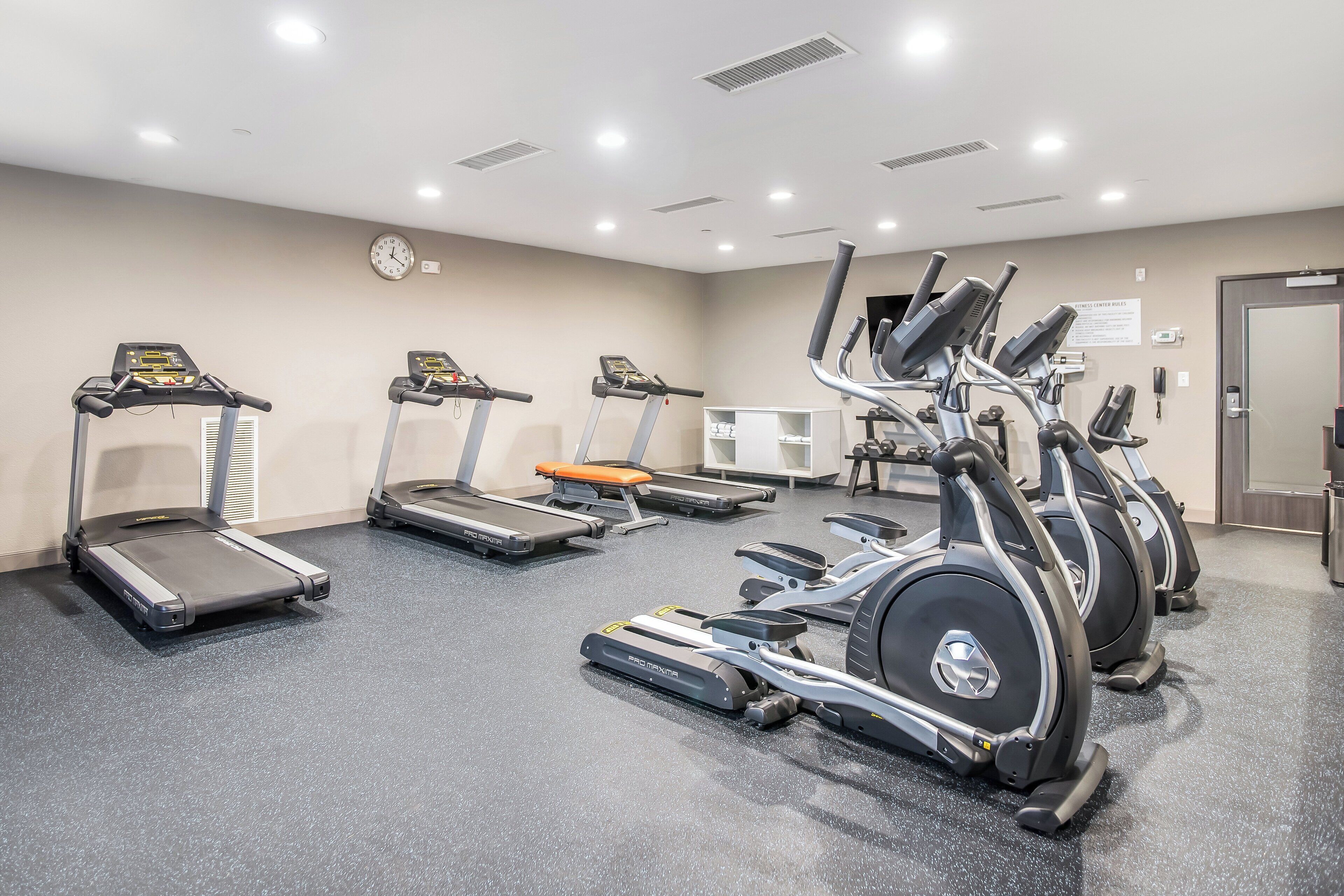 A fitness center with treadmills, elliptical machines, and a wall clock.