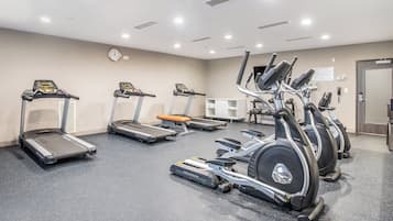 A fitness center with treadmills, elliptical machines, and a wall clock.