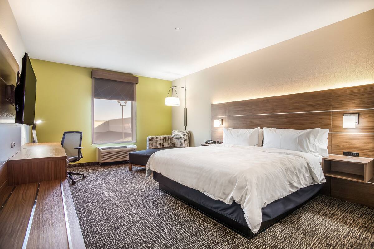 Habitación de hotel con una cama grande, un escritorio, una silla, un televisor de pantalla plana y una ventana con vistas.