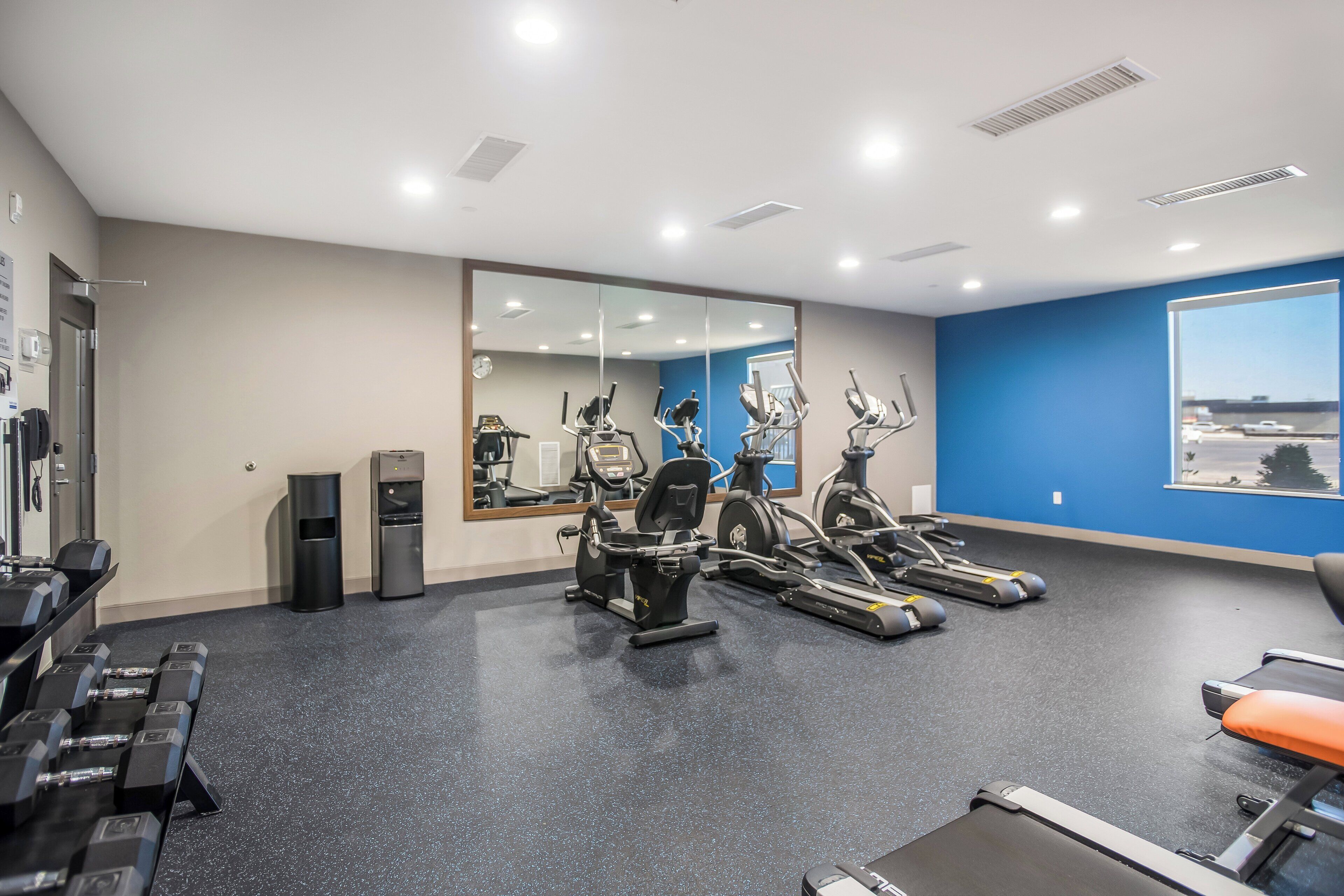 Ein Fitnessstudio mit Trainingsgeräten, einem Wasserspender und einem großen Spiegel.