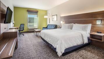 A hotel room with a large bed, a desk, a chair, a TV, and a window with blinds.