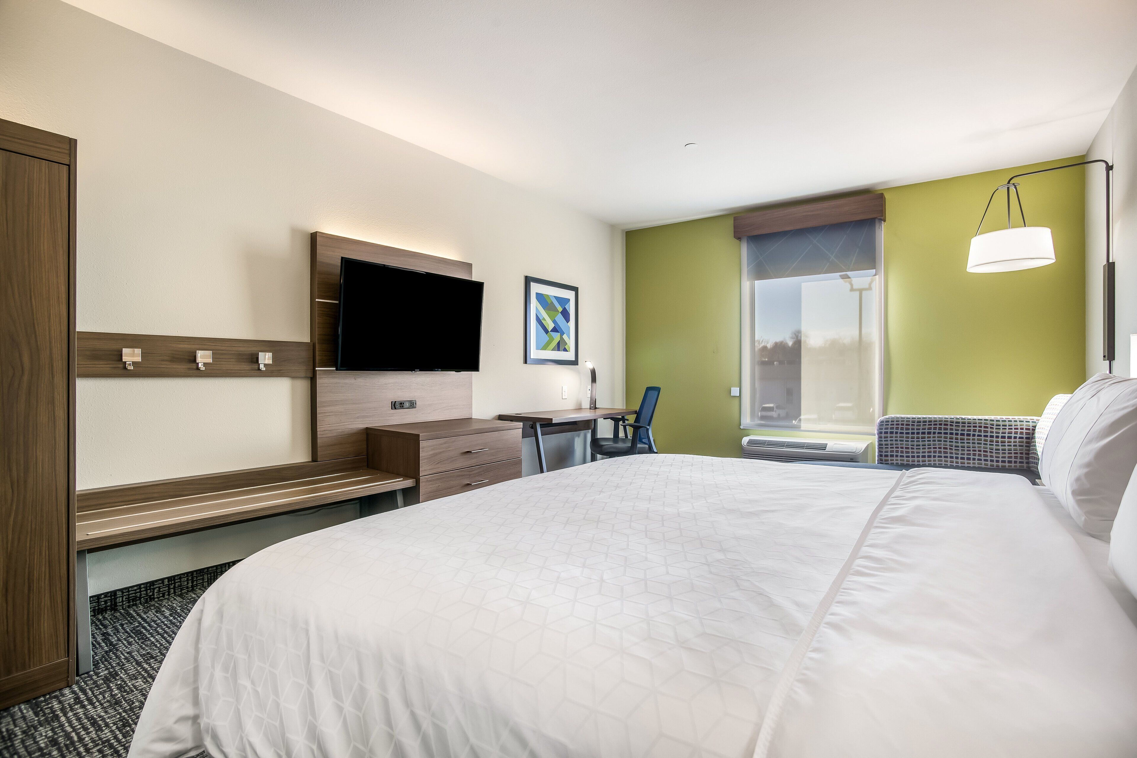 A hotel room with a large bed, a desk with a chair, a flat-screen TV, and a window with a view.