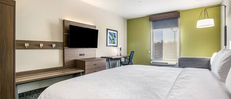 A hotel room with a large bed, a desk with a chair, a flat-screen TV, and a window with a view.