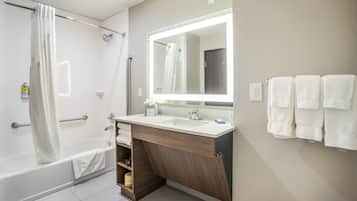 A modern bathroom with a bathtub, a large mirror, a sink, and a towel rack.