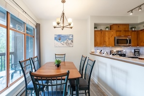 Un coin repas avec une table et des chaises en bois, un lustre et un tableau représentant une montagne accroché au mur.