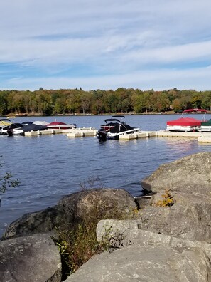 A calm lake with boats docked at a pier, surrounded by rocky terrain and trees.