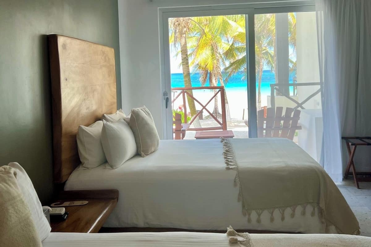 Ein Schlafzimmer mit zwei Betten, einem Holzkopfende und Blick auf den Strand sowie Palmen durch eine Glastür.