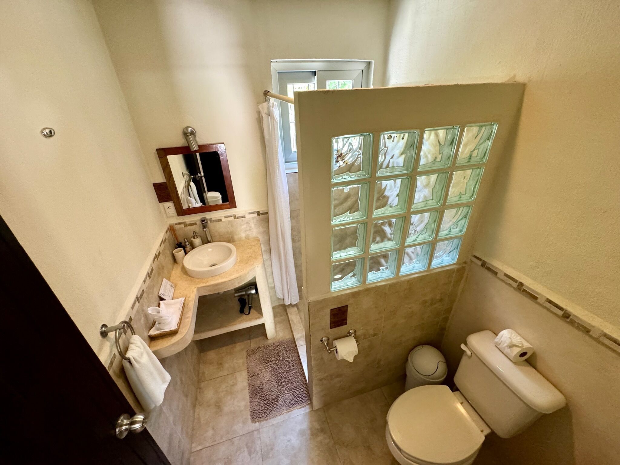 A compact bathroom with a sink, mirror, toilet, and a window with a view.