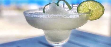 Un cóctel margarita en una copa de tallo, adornado con una rodaja de lima, sobre una mesa de madera azul.