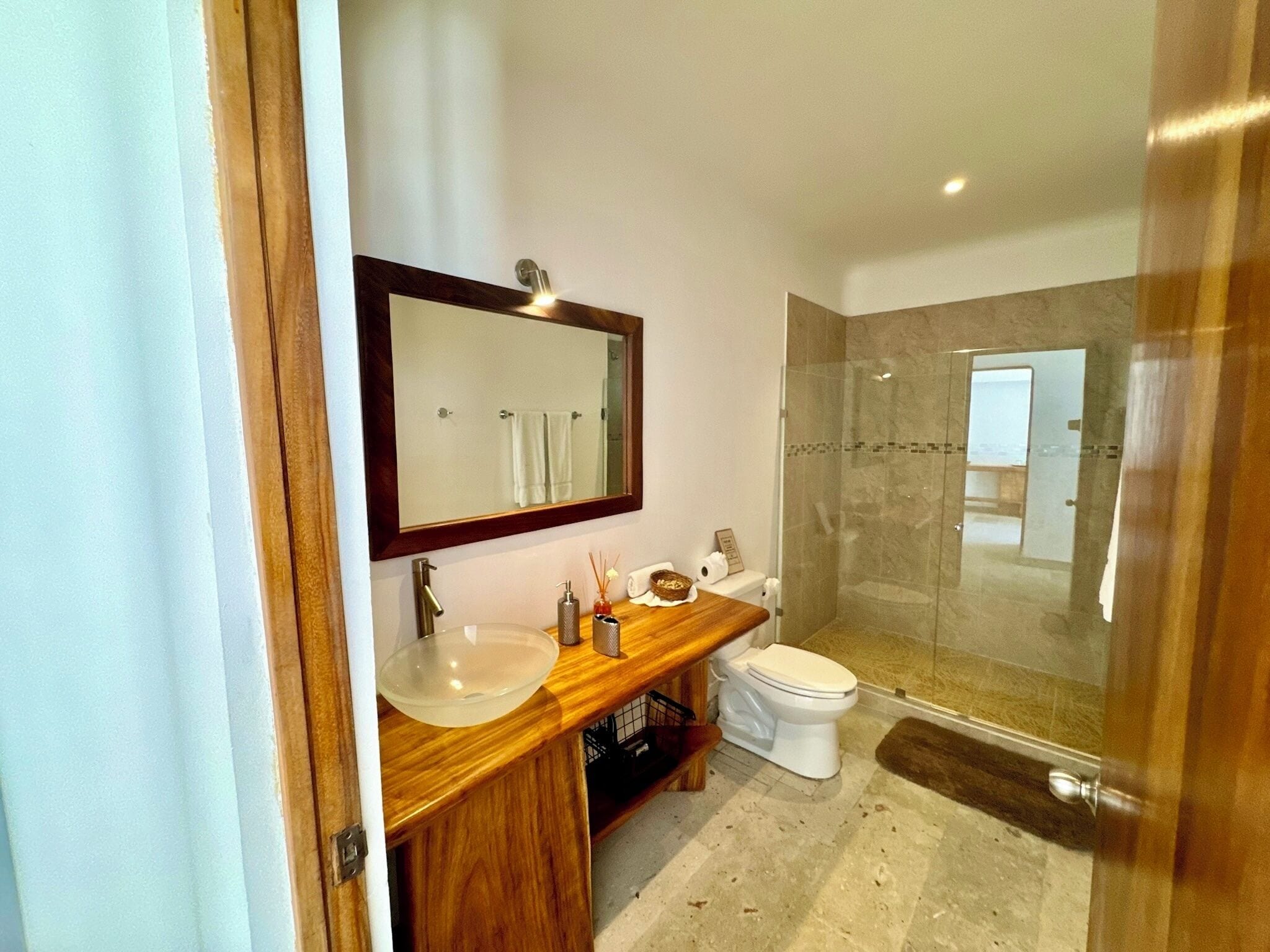 A modern bathroom with a wooden vanity, a large mirror, a glass shower enclosure, and a white toilet.