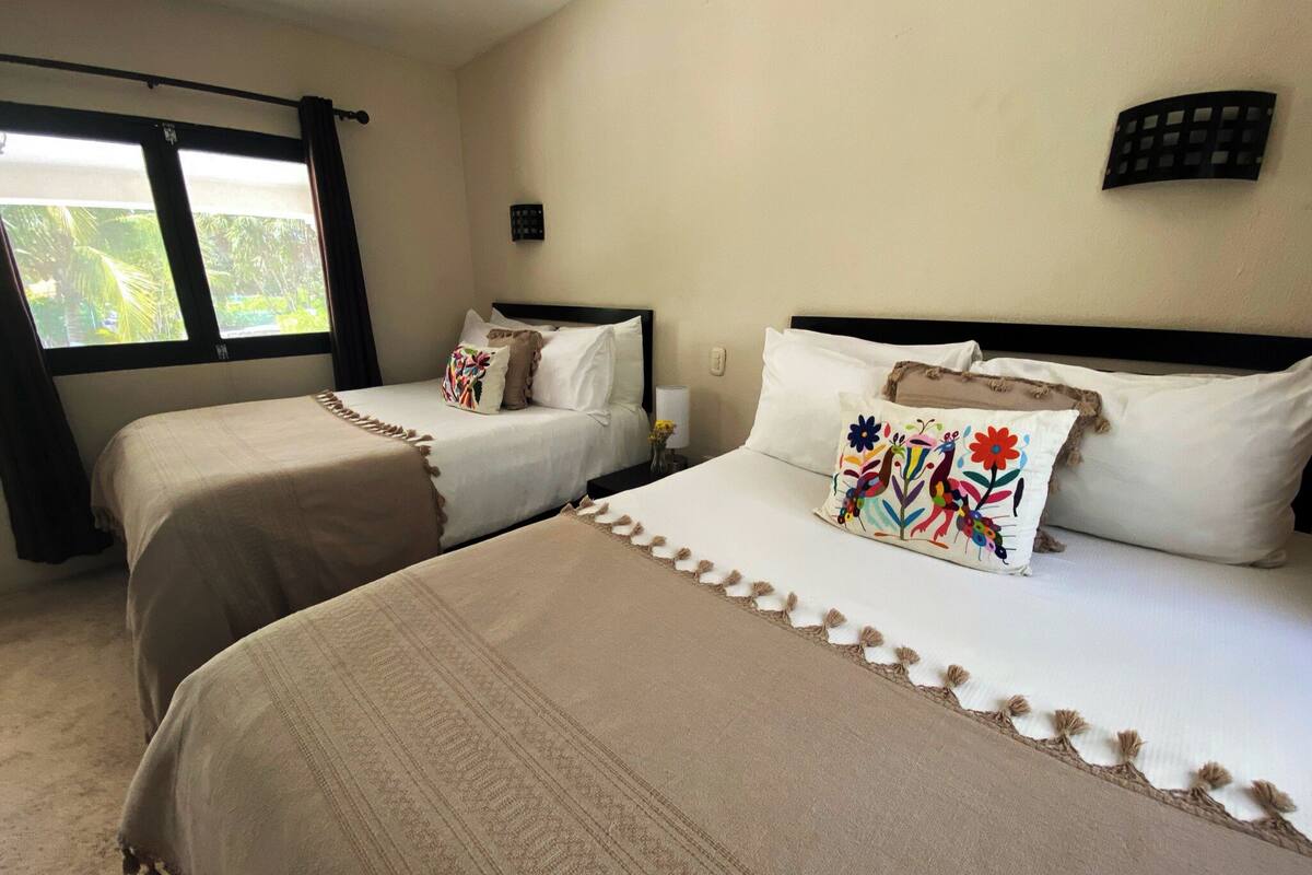 Ein Hotelzimmer mit zwei Betten, beiger Bettwäsche und einem Fenster mit Vorhängen.