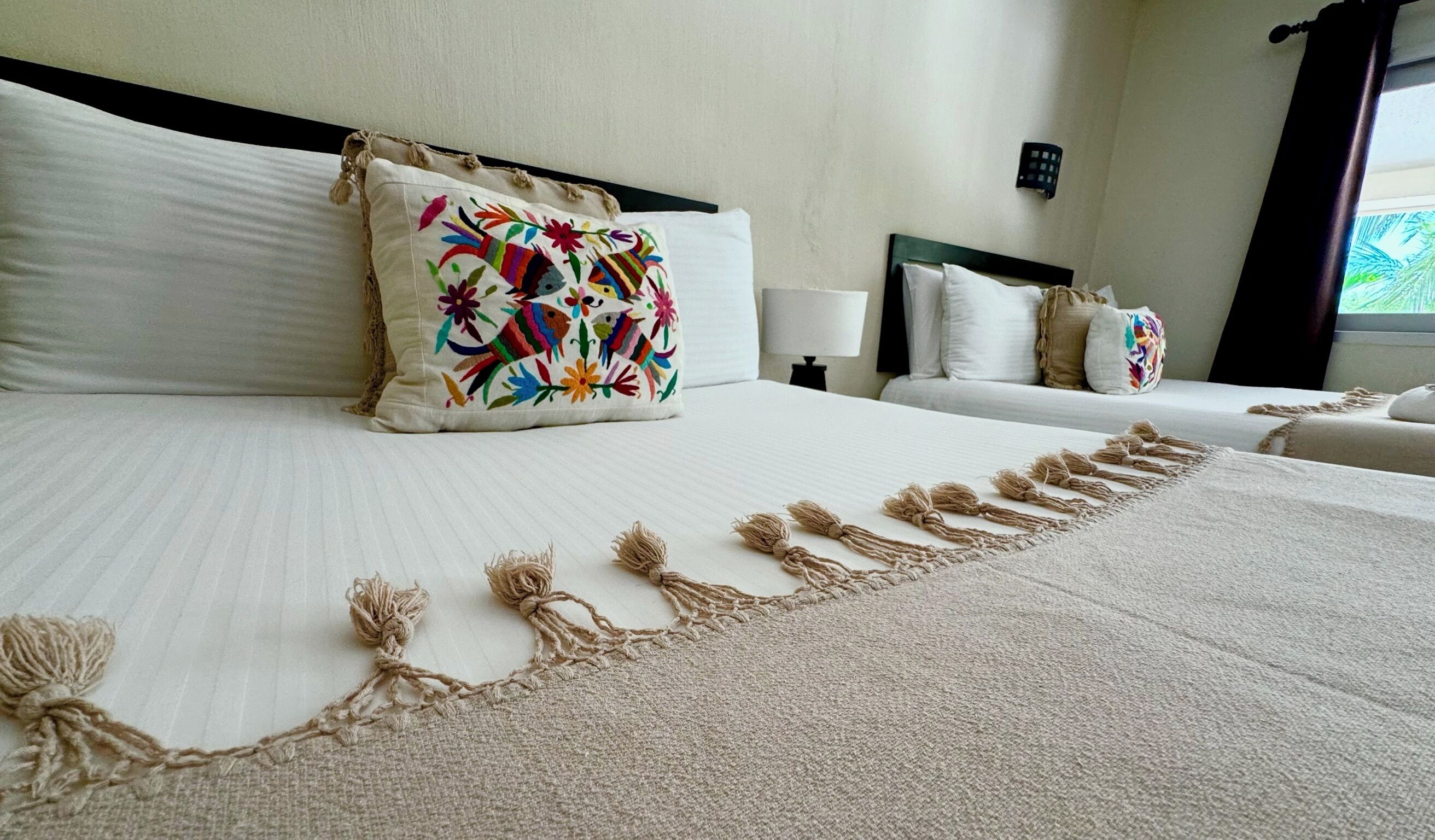 A hotel room with a large bed, two pillows, a bedside table, and a window with curtains.