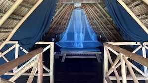 Une tente à toit de chaume, avec un lit et une lanterne suspendue.