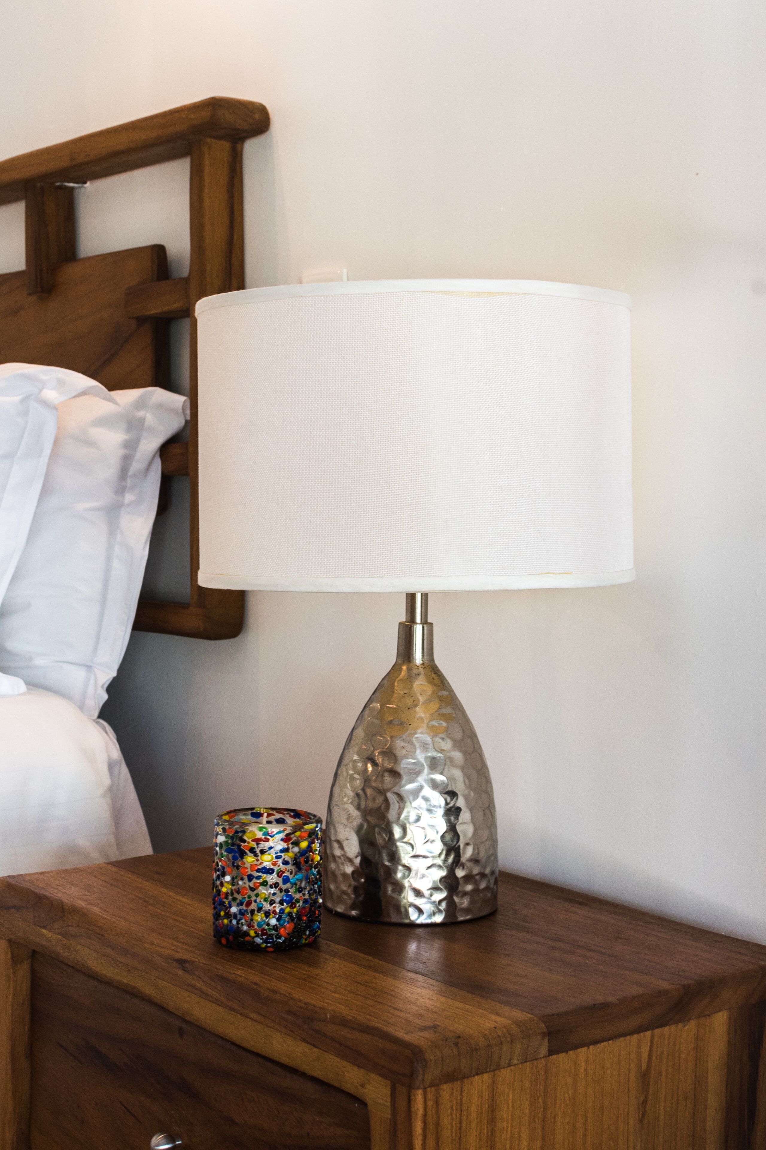 Un comodino in legno con una lampada e una tazza colorata.