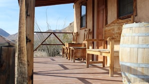 A wooden deck with a wooden table and chairs, a wooden barrel, and a building with windows and a door.