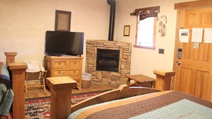 A cozy room with a stone fireplace, a television on a wooden dresser, a wooden door, and a patterned rug.