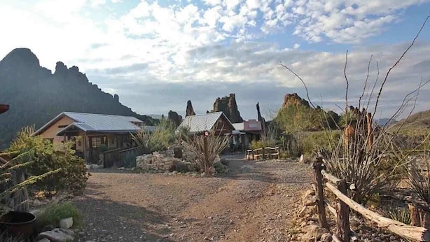 A rustic cabin with a metal roof, surrounded by dry vegetation and rocky terrain.